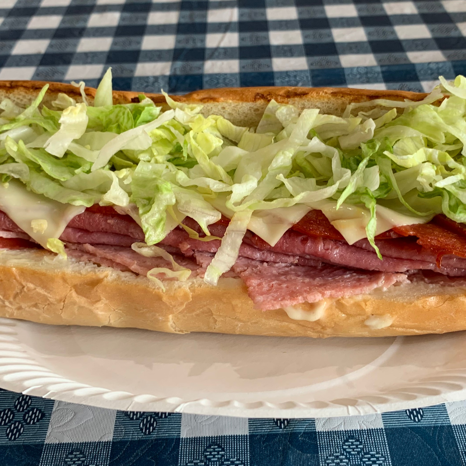 A Ginos Pizza and Grill sub sandwich with meat, cheese, and shredded lettuce on a white paper plate.